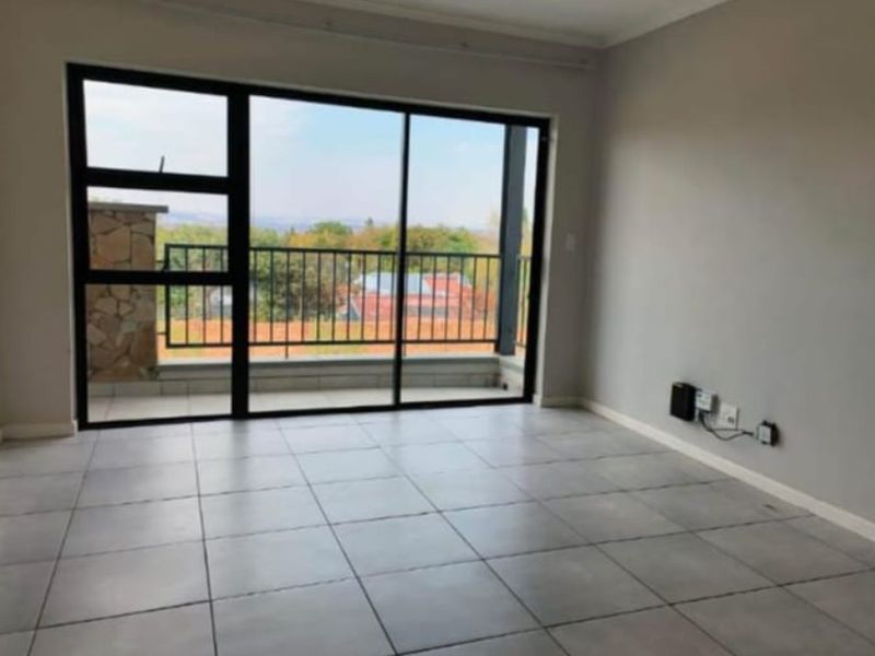 A bright, empty living room featuring neutral tiled flooring and large sliding glass doors that open onto a balcony with scenic views.