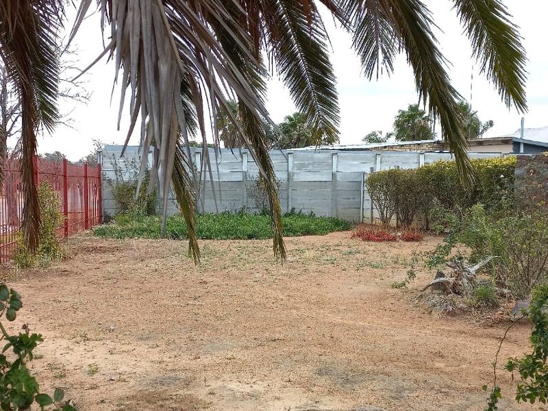 A spacious garden area featuring a mix of stone and precast concrete boundary walls with red metal perimeter fencing.