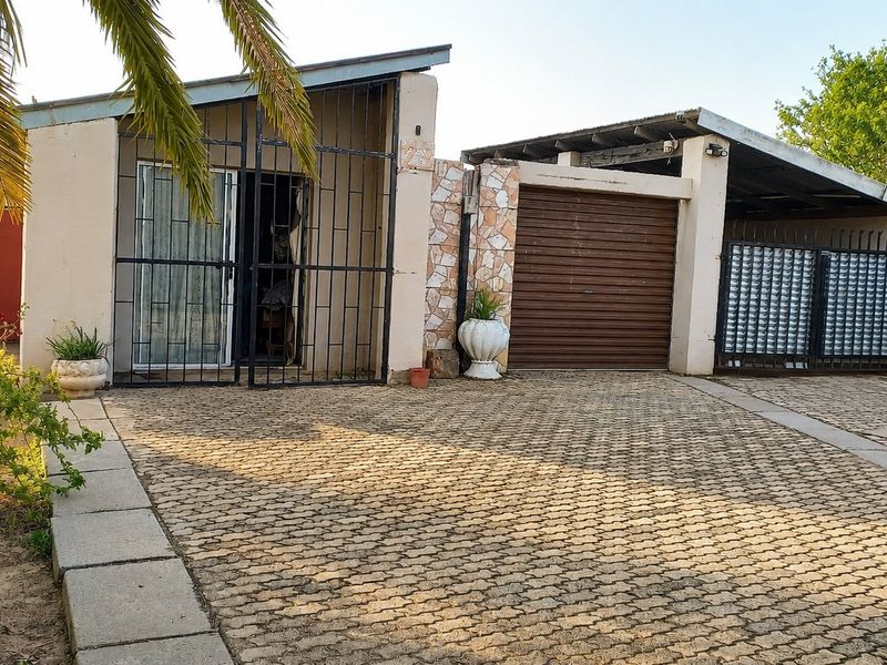 Front elevation of the property featuring a paved driveway, secure gated entrance, roller garage door, and a covered carport area.