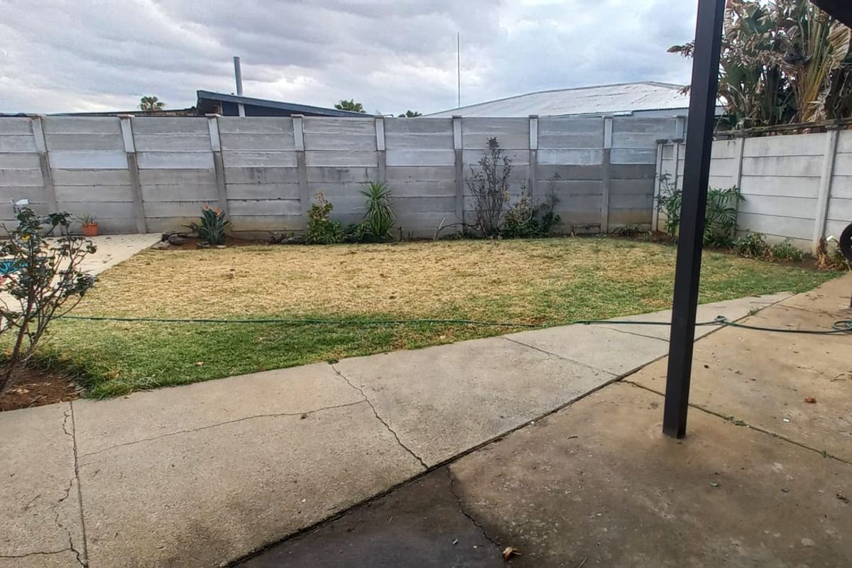 Rear garden area featuring a concrete patio, swimming pool, and precast concrete boundary wall, requiring landscaping and surface maintenance.
