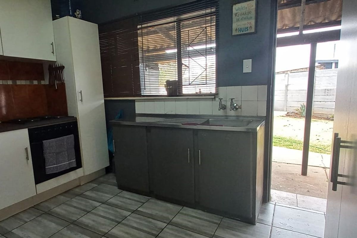 A functional kitchen featuring built-in cabinetry, a stainless steel sink, integrated oven and hob, with direct access to the rear garden area.