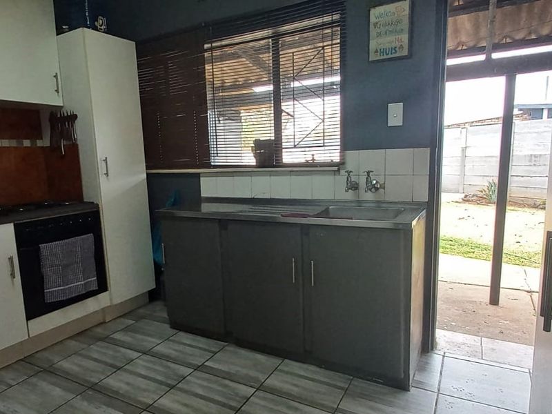 A functional kitchen featuring built-in cabinetry, a stainless steel sink, integrated oven and hob, with direct access to the rear garden area.