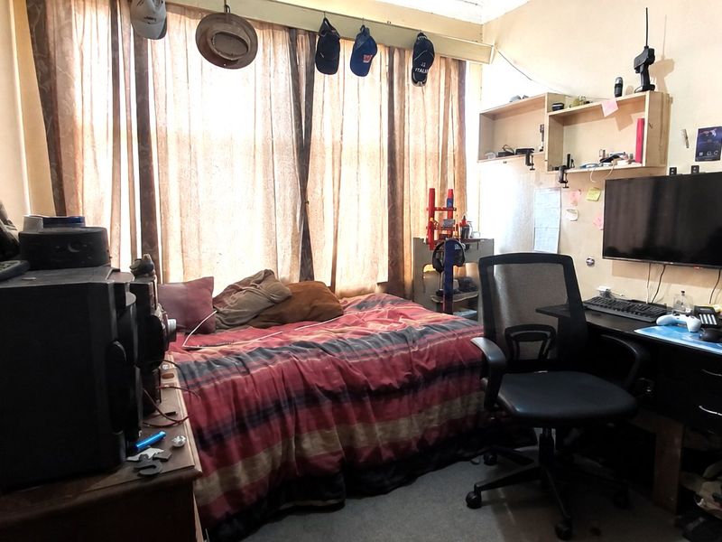 A compact bedroom featuring built-in shelving and large window coverage, currently utilized as a multi-purpose living and workspace.