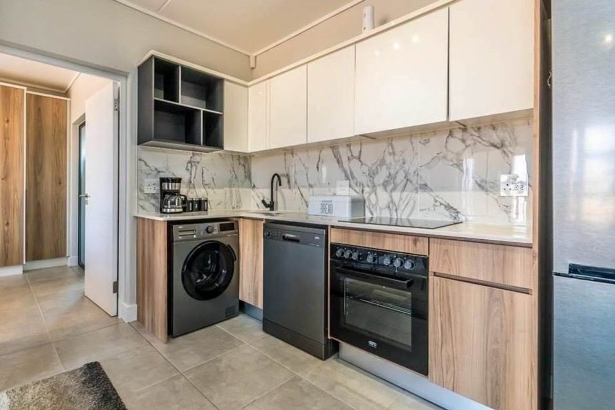 Modern kitchen featuring sleek white and wood-grain cabinetry, marble-look splashback, built-in oven, hob, and integrated laundry and dishwasher appliances.