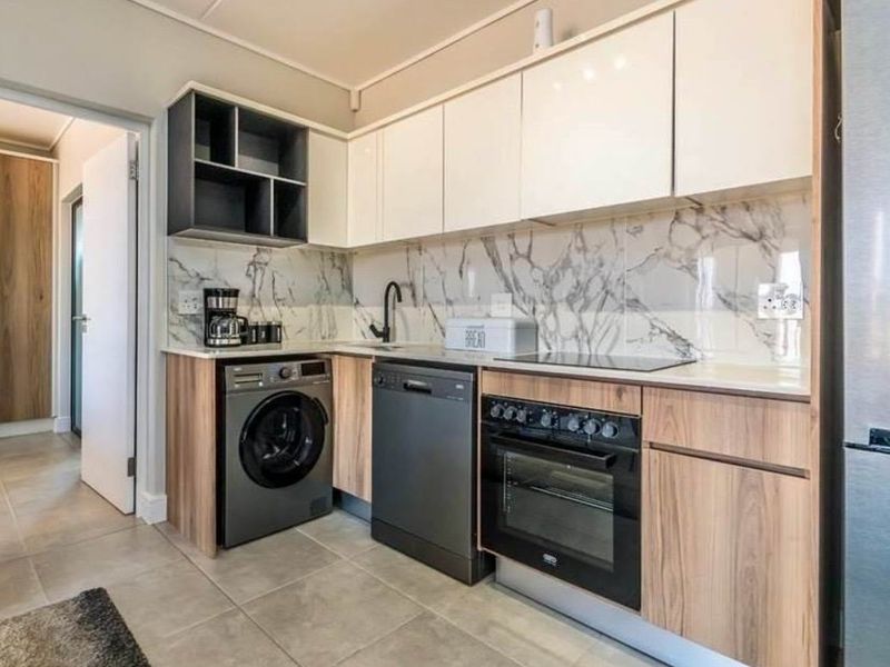 Modern kitchen featuring sleek white and wood-grain cabinetry, marble-look splashback, built-in oven, hob, and integrated laundry and dishwasher appliances.