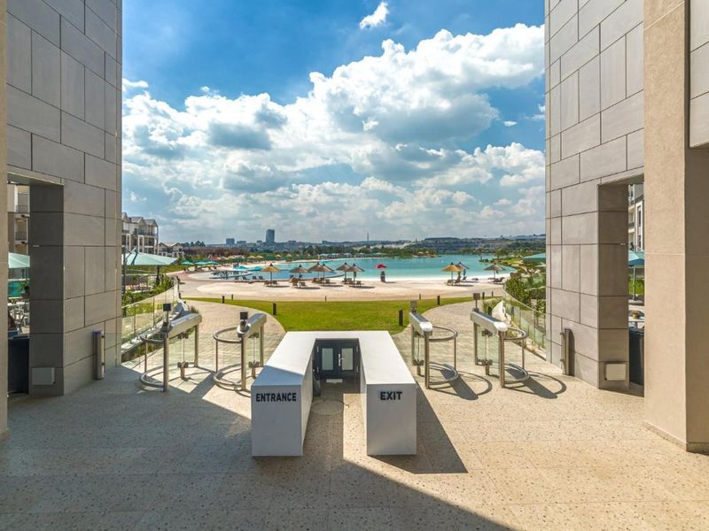 A view through the apartment complex entrance towards a large communal swimming pool and landscaped recreational area.