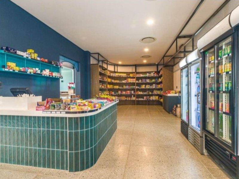 A well-maintained commercial retail space featuring a tiled service counter, extensive built-in shelving, and integrated commercial refrigeration units.