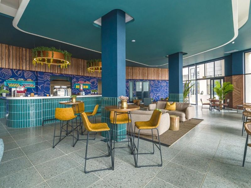 A modern, vibrant open-plan communal area featuring a tiled bar counter, structural columns, and contemporary finishes, ideal for social gatherings or casual dining.