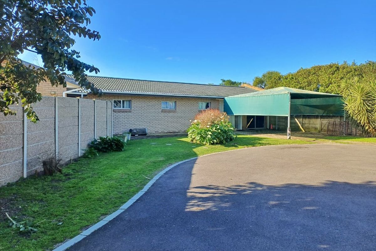 Rear view of the property featuring a brick facade, tiled roof, attached carport, and a spacious garden area with a paved driveway.