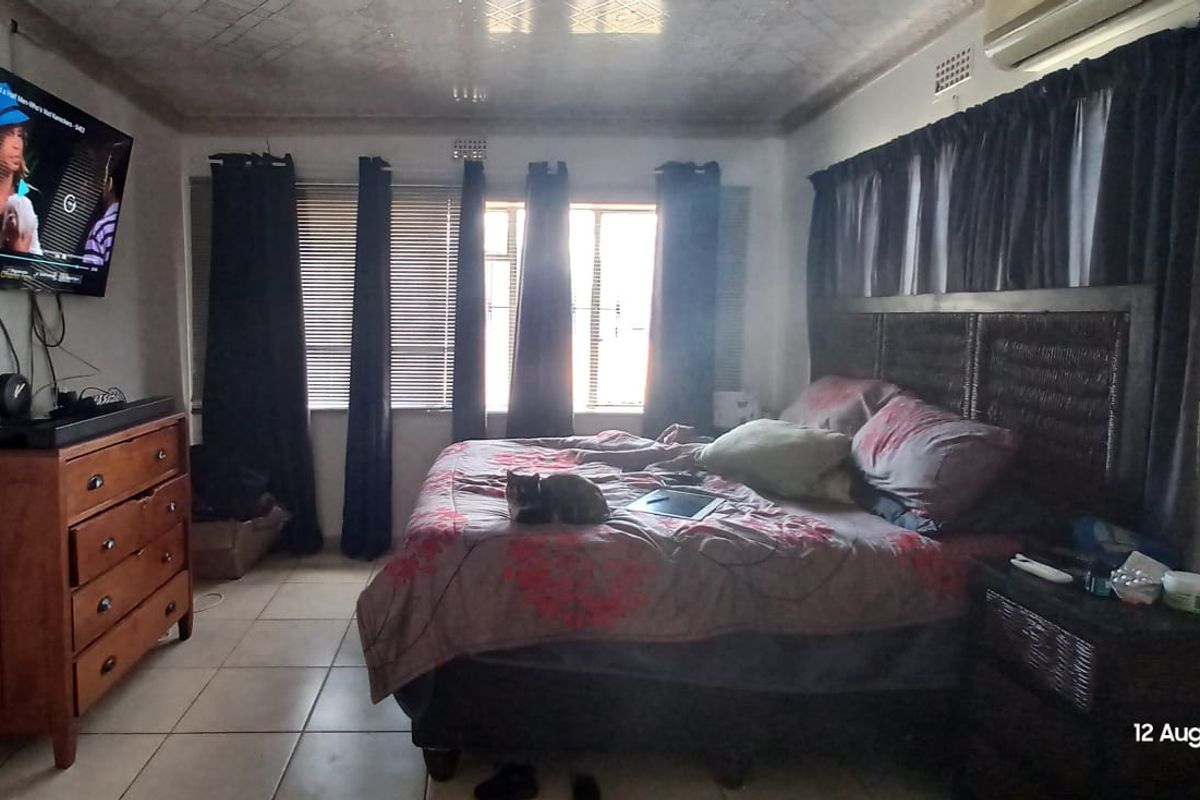 A bedroom featuring tiled flooring and a wall-mounted air conditioning unit, with visible signs of ceiling wear and staining.