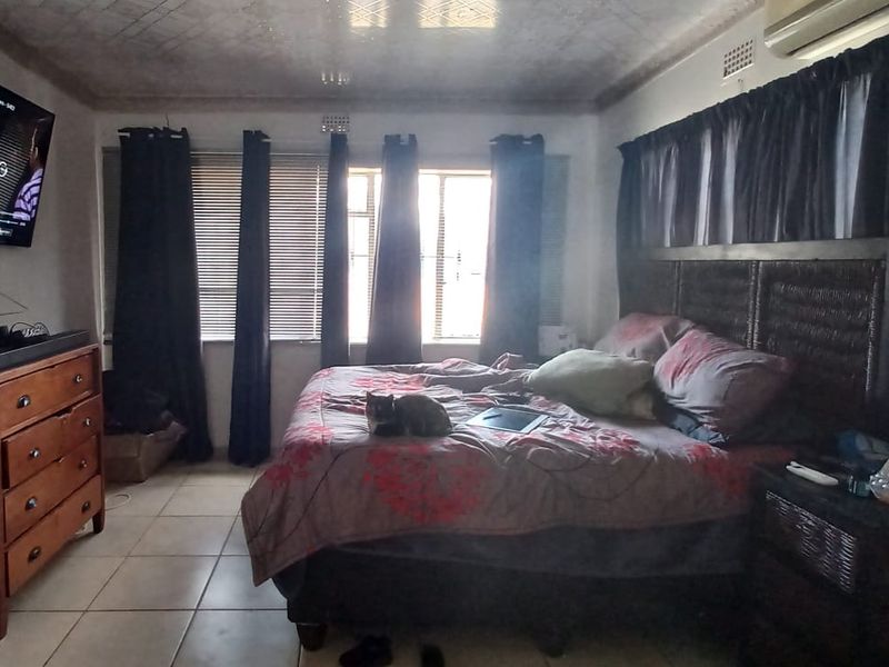 A bedroom featuring tiled flooring and a wall-mounted air conditioning unit, with visible signs of ceiling wear and staining.