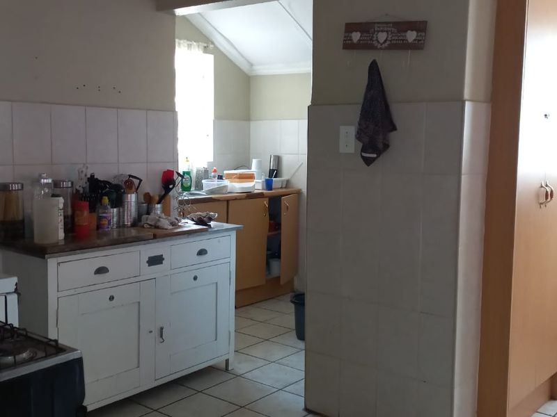A functional kitchen space featuring tiled splashbacks, built-in cabinetry, and tiled flooring, offering potential for modernization and aesthetic updates.