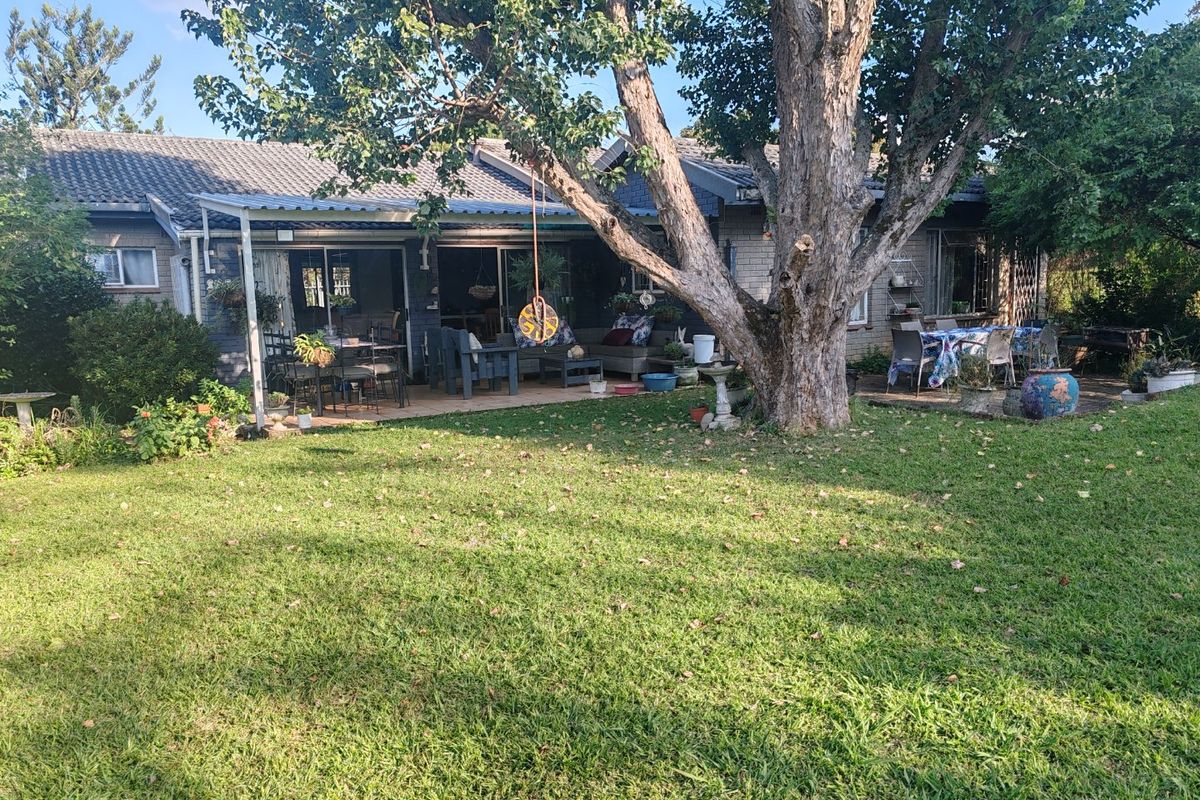 A view of the rear garden featuring a large mature tree, a paved patio area, and a covered outdoor space attached to the house.