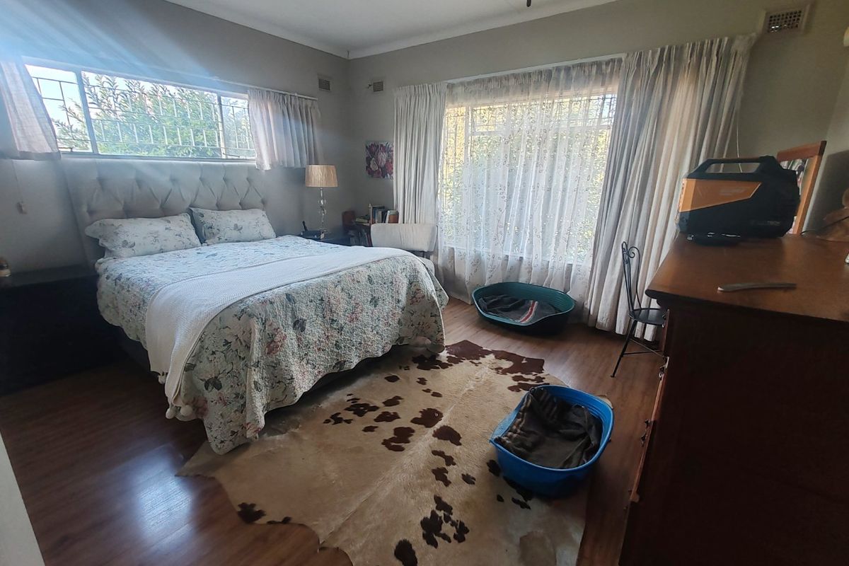 A spacious bedroom featuring laminate flooring, large windows with burglar bars, and neutral wall finishes, offering a comfortable and functional living space.