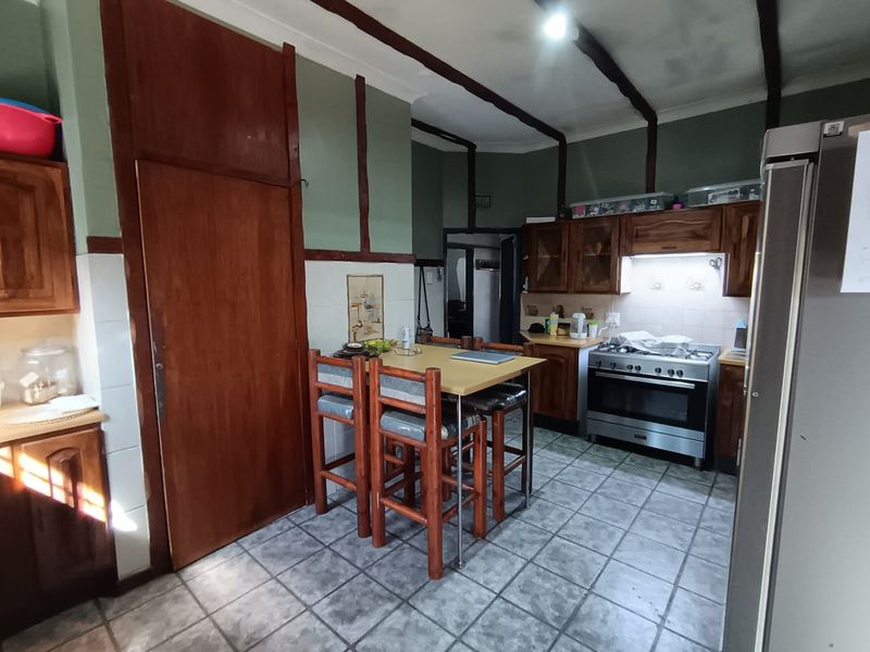 A dated kitchen featuring wooden cabinetry, tiled flooring, and a gas stove with an integrated extractor fan.