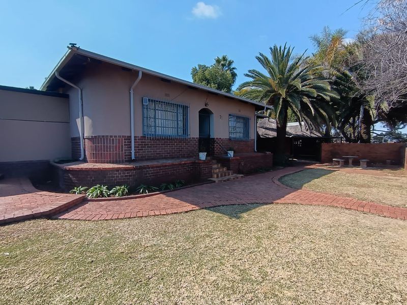 Front view of a single-story brick house featuring a paved walkway, security bars on windows, and a landscaped garden area.