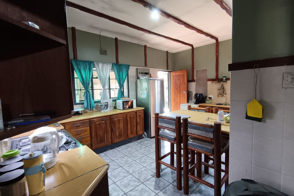 A functional kitchen featuring wooden cabinetry, tiled flooring, and exposed ceiling beams, offering a traditional layout with ample counter space and integrated fixtures.