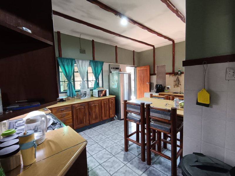 A functional kitchen featuring wooden cabinetry, tiled flooring, and exposed ceiling beams, offering a traditional layout with ample counter space and integrated fixtures.