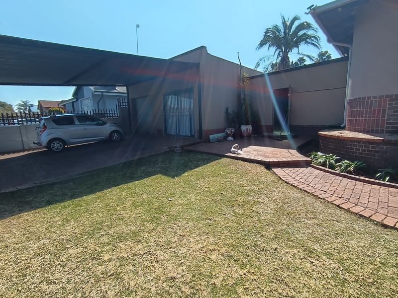 Front exterior view of the house featuring a paved driveway, carport, and a small front garden area.