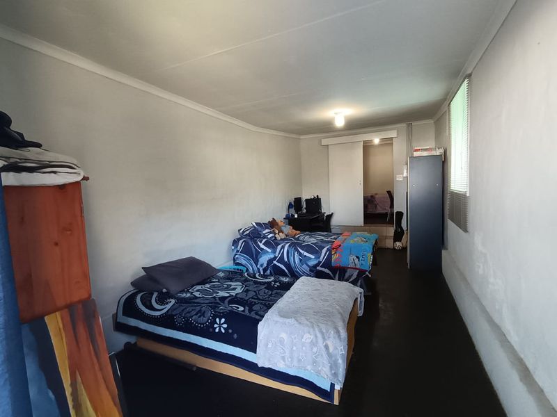 A bedroom featuring a coved ceiling, sliding door access to an adjacent room, and window blinds, showing signs of wear on the wall surfaces.