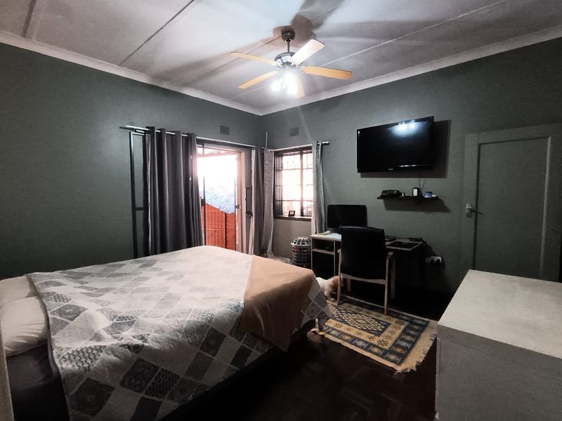 A bedroom featuring dark green walls, a ceiling fan, hardwood flooring, and a sliding door providing access to an outdoor area.