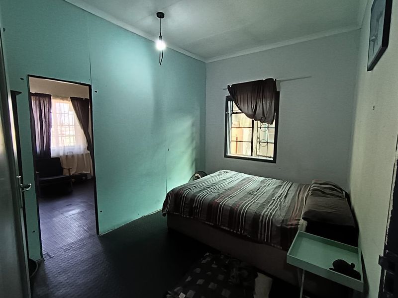 A bedroom featuring a window with security bars and a pendant light, showing signs of wear on the walls and flooring.