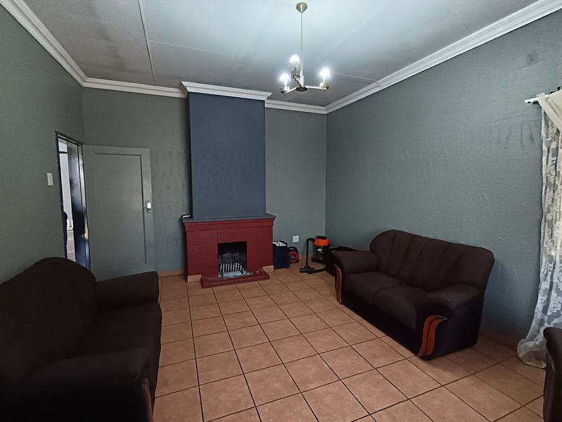 A living room featuring a central brick fireplace, tiled flooring, and decorative ceiling cornices.