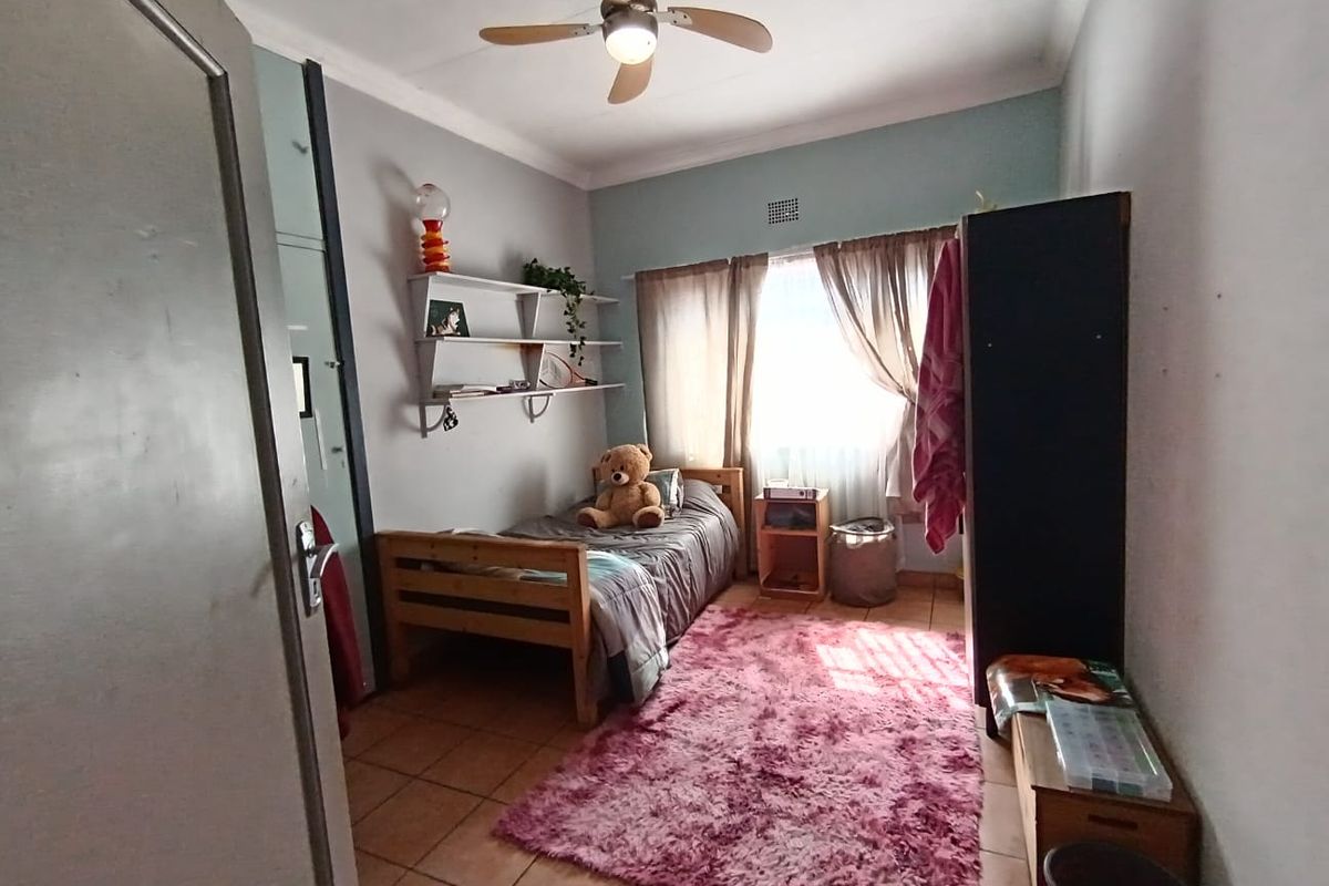 A functional bedroom featuring tiled flooring, a ceiling fan, and built-in wall shelving, offering a practical space with natural light.