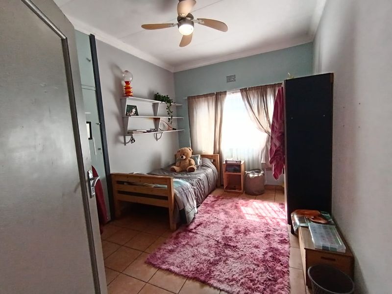 A functional bedroom featuring tiled flooring, a ceiling fan, and built-in wall shelving, offering a practical space with natural light.