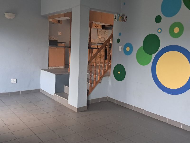 An open-plan living area featuring tiled flooring, a wooden staircase leading to a kitchen space, and decorative wall paint.