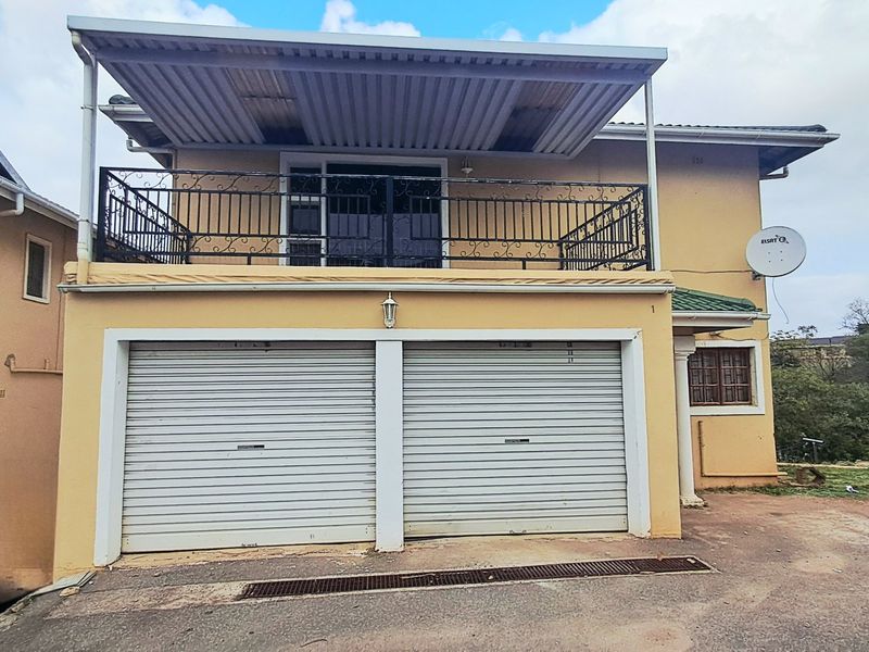 Front elevation of the property featuring a double garage with roller shutter doors and an upper-level balcony with wrought iron railings.