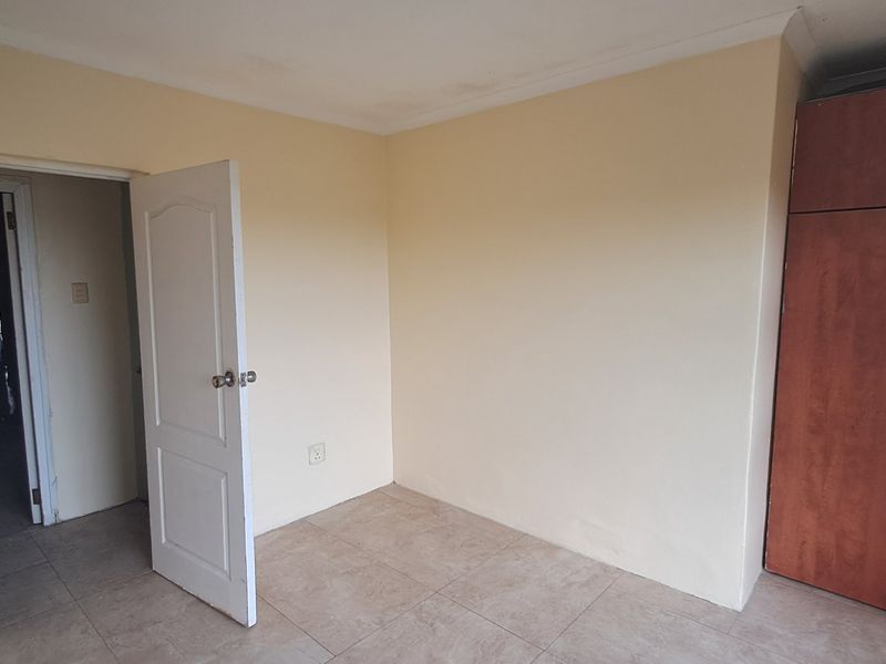 An empty bedroom featuring tiled flooring, built-in wooden cupboards, and neutral wall finishes, offering a blank canvas for personalization.