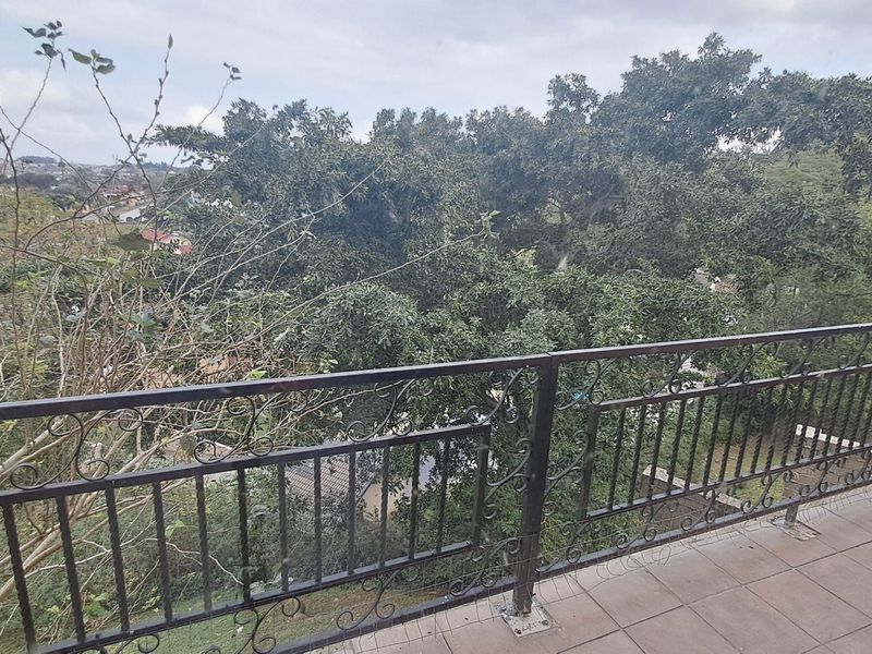 A balcony featuring tiled flooring and a decorative wrought iron railing, offering an elevated view of the surrounding trees and neighborhood.