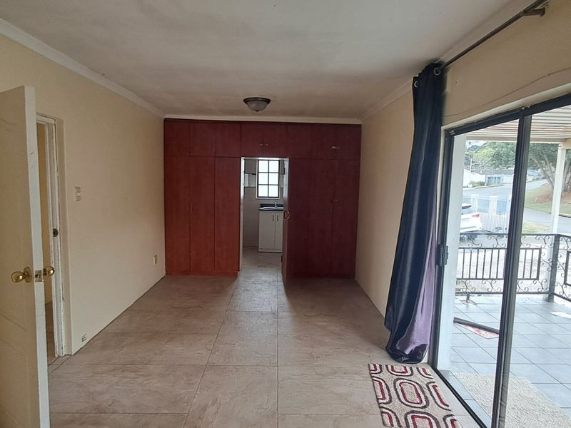An empty living area featuring tiled flooring, built-in storage cupboards, and a sliding glass door providing access to an outdoor patio.