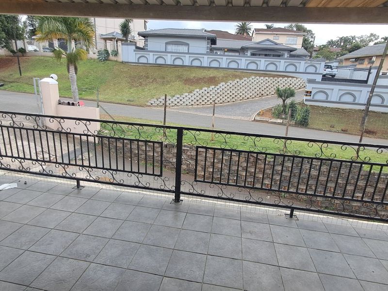 A covered balcony featuring tiled flooring and a decorative wrought iron balustrade, overlooking the street and surrounding residential area.