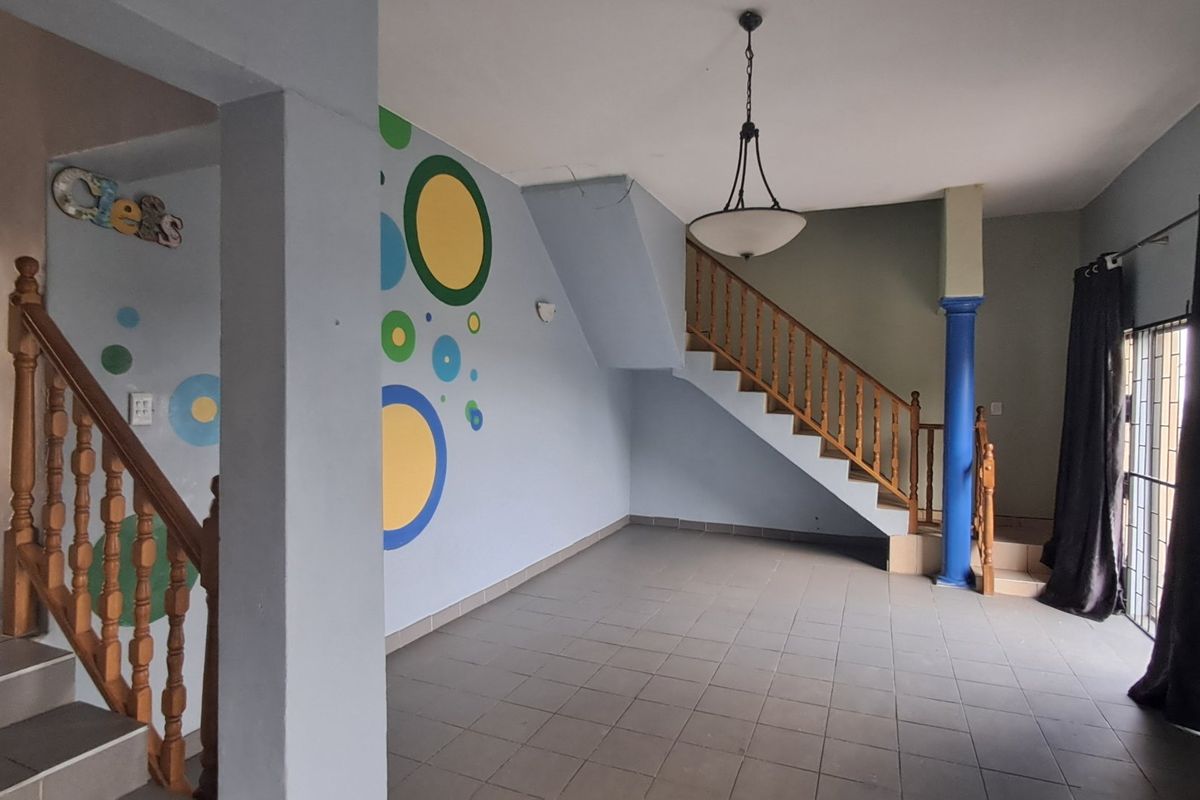 An open-plan living area featuring a staircase with a wooden balustrade, tiled flooring, and a central pendant light fixture.