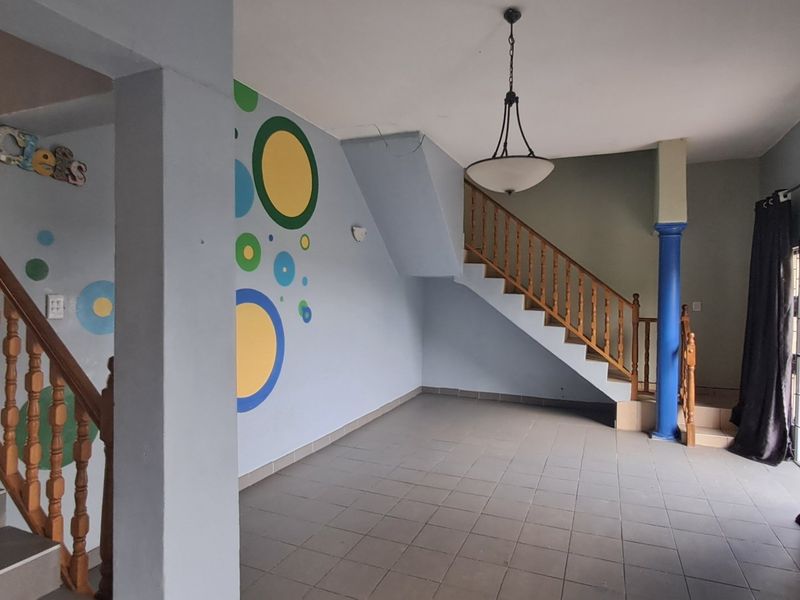 An open-plan living area featuring a staircase with a wooden balustrade, tiled flooring, and a central pendant light fixture.