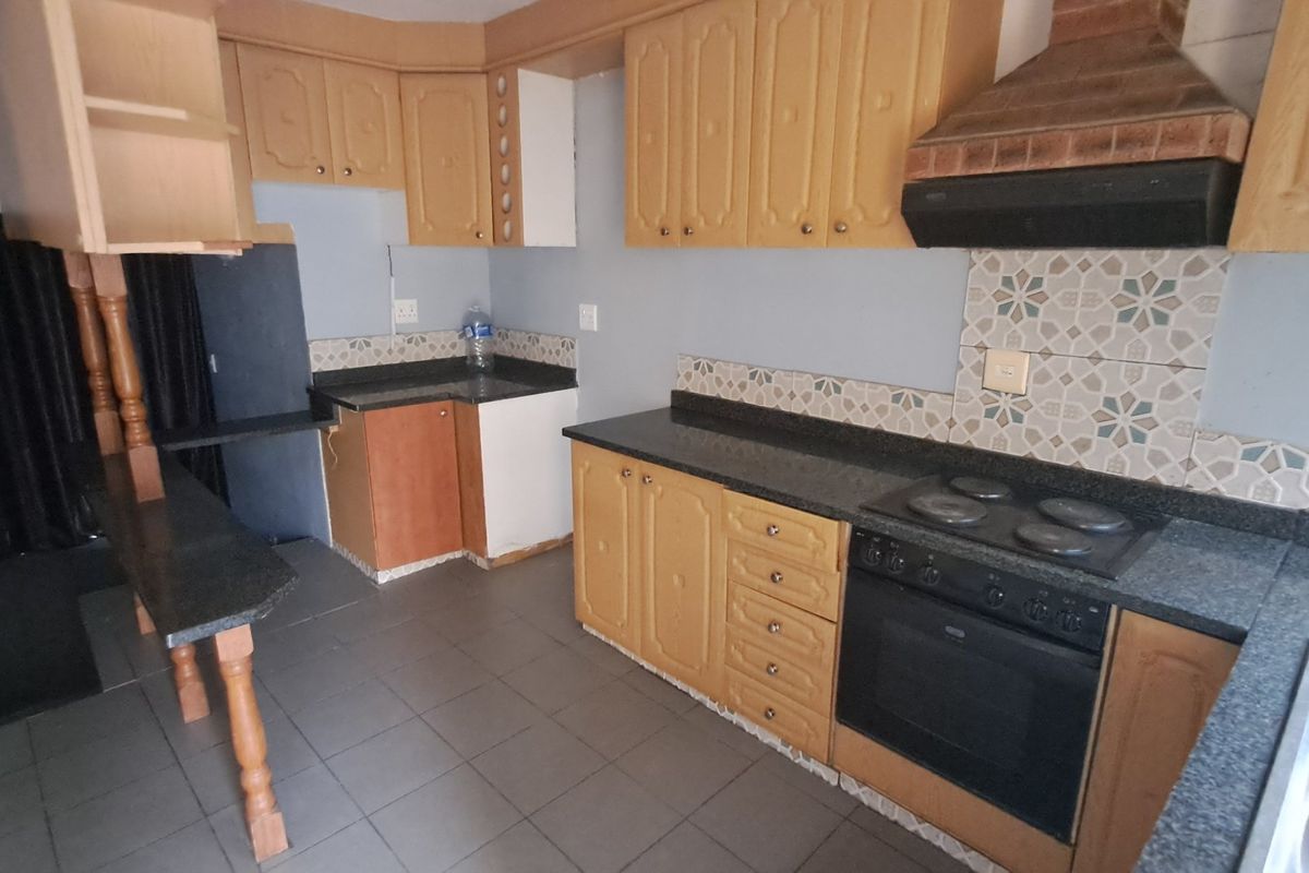 A dated kitchen featuring wooden cabinetry, granite countertops, built-in oven, and hob, with tiled flooring and backsplash, offering potential for modernization.
