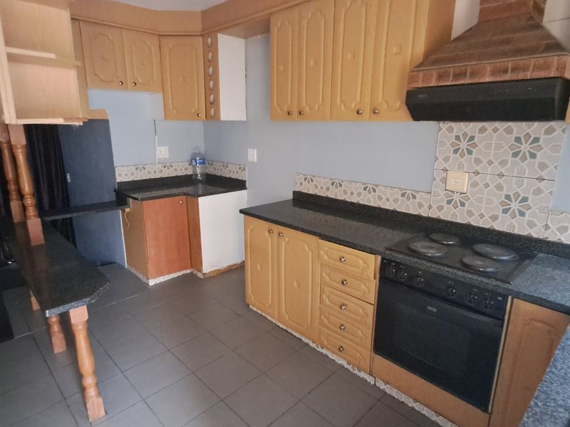 A dated kitchen featuring wooden cabinetry, granite countertops, built-in oven, and hob, with tiled flooring and backsplash, offering potential for modernization.