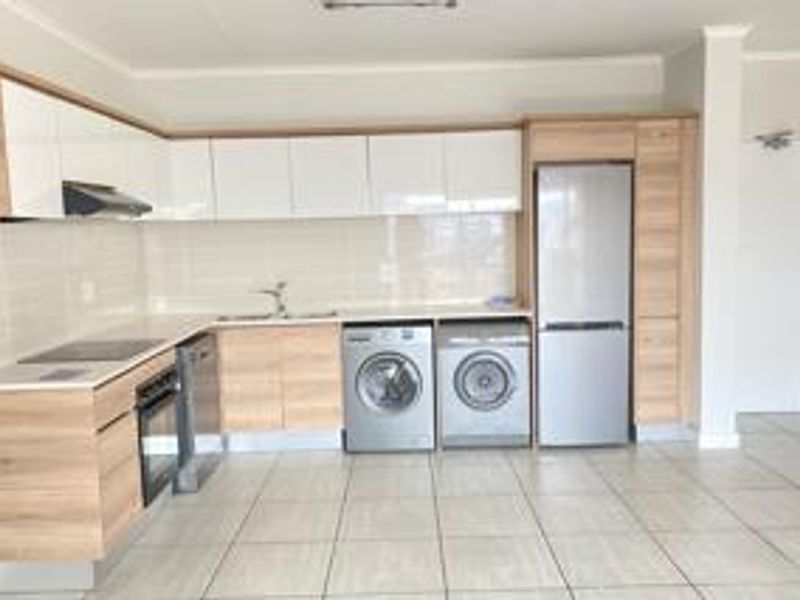 Modern kitchen featuring light wood-tone cabinetry, white high-gloss upper cabinets, tiled backsplash, and integrated appliance spaces with neutral tiled flooring.