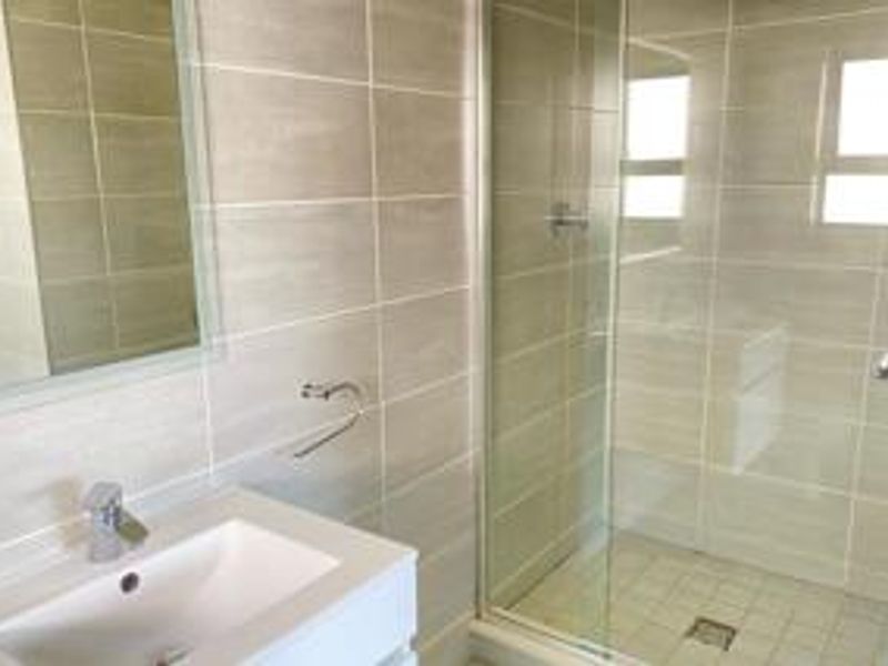 A modern bathroom featuring a vanity basin with mixer tap, wall mirror, and a glass-enclosed shower with neutral wall and floor tiling.