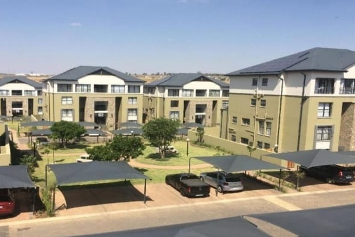 An elevated view of a modern apartment complex featuring multiple residential blocks, paved driveways, shade cloth carports, and well-maintained communal garden areas.