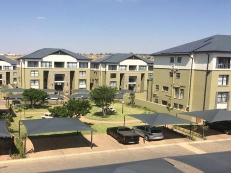 An elevated view of a modern apartment complex featuring multiple residential blocks, paved driveways, shade cloth carports, and well-maintained communal garden areas.