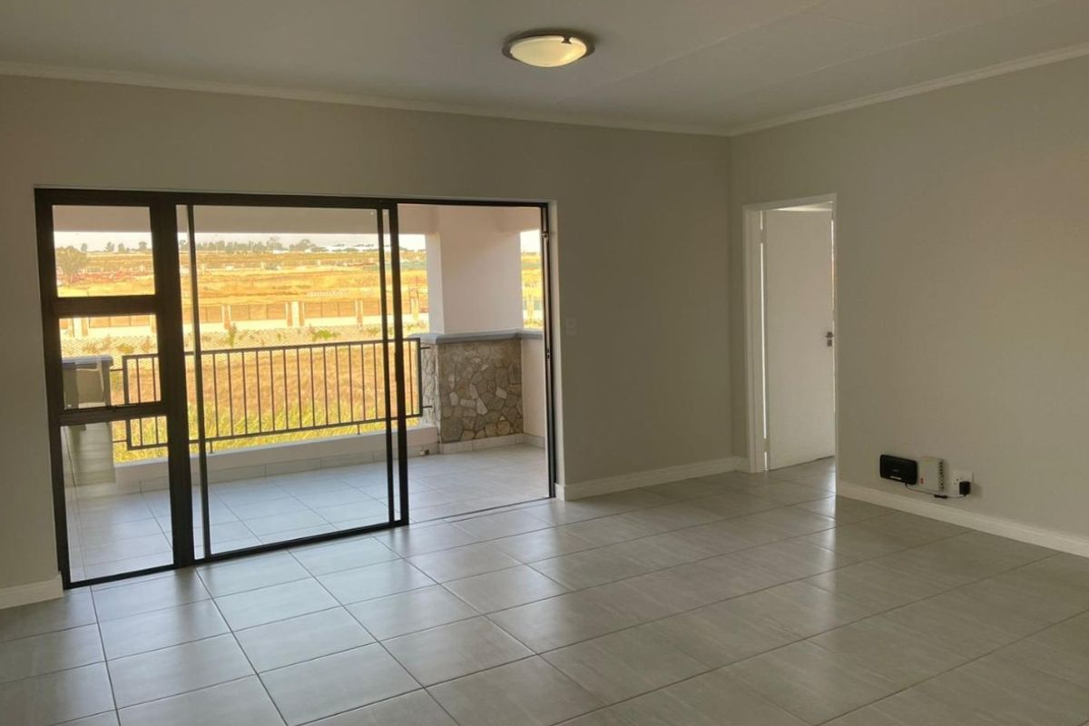 Spacious, light-filled living area featuring neutral tiled flooring and large sliding glass doors that open onto a private balcony.