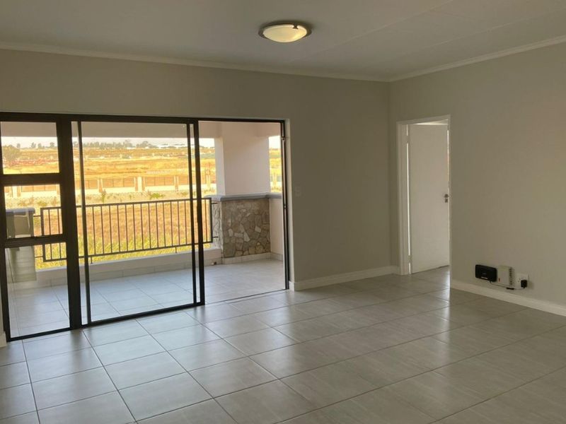Spacious, light-filled living area featuring neutral tiled flooring and large sliding glass doors that open onto a private balcony.