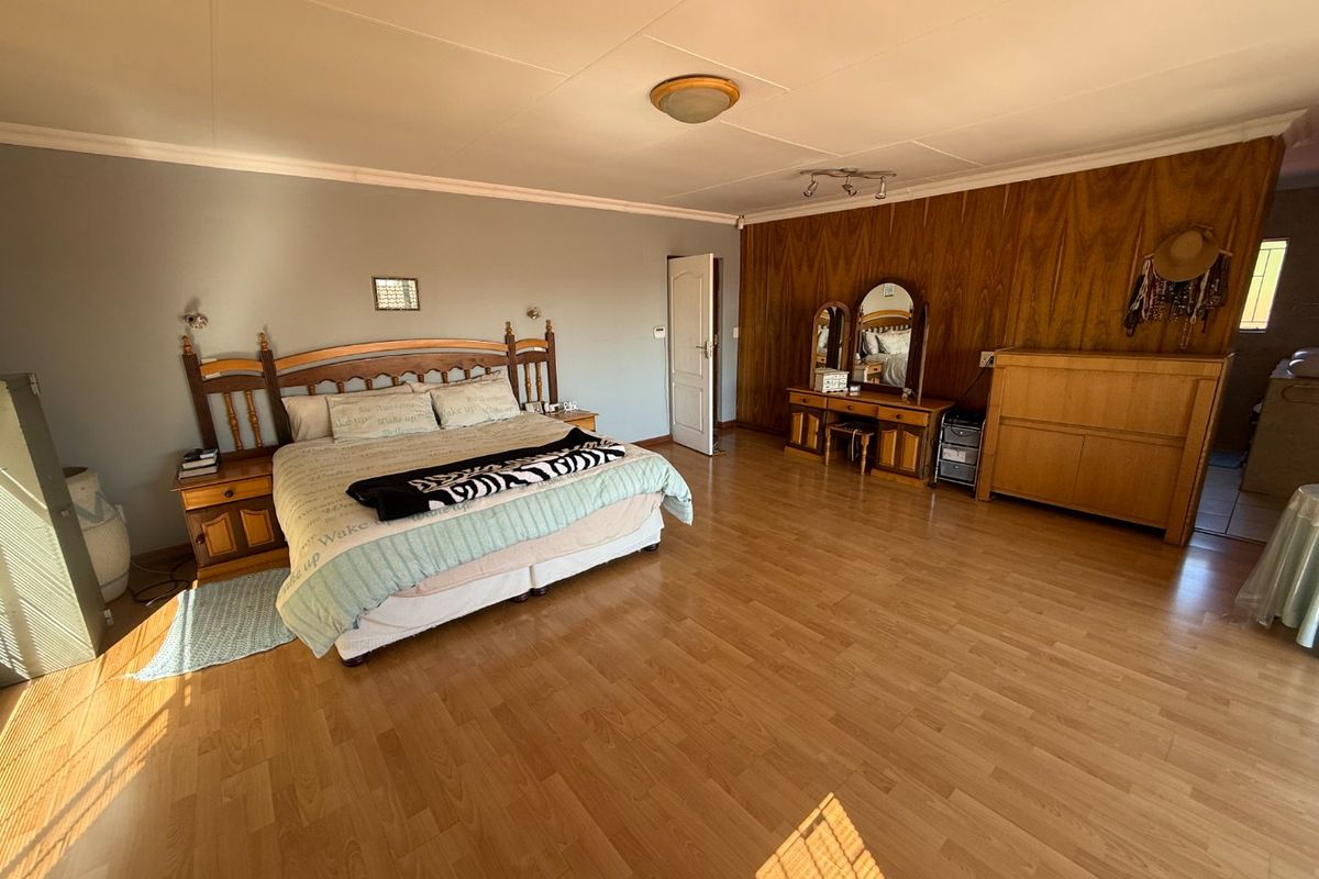 Spacious bedroom featuring laminate flooring, a wood-paneled accent wall, and dual lighting fixtures, offering a functional layout with ample room for furniture.