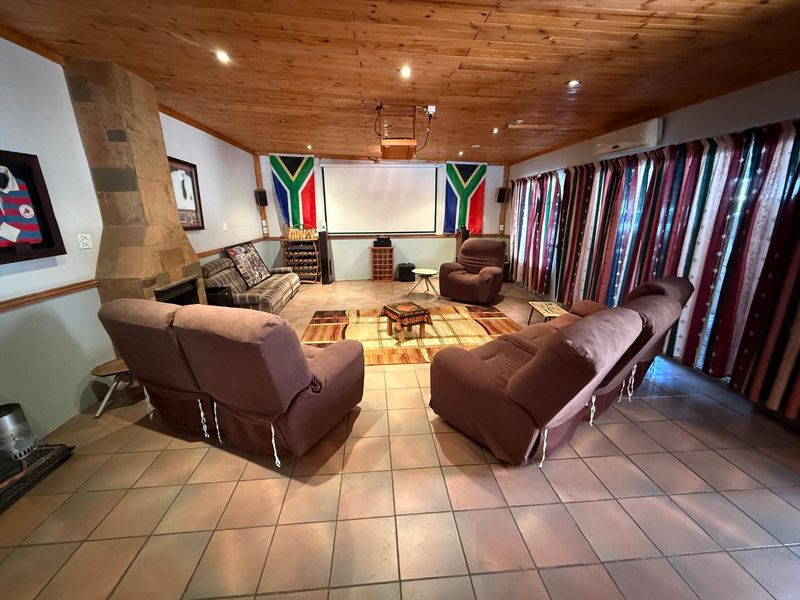 A dedicated cinema room featuring a stone fireplace, timber-clad ceiling, tiled flooring, and a large projector screen for home entertainment.