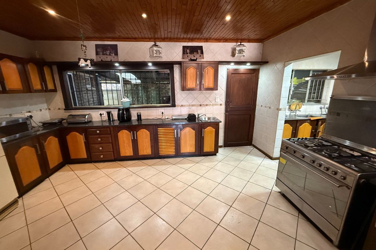 Spacious kitchen featuring timber ceilings, tiled flooring, built-in cabinetry, and a gas stove with extractor fan, with an adjacent scullery area.