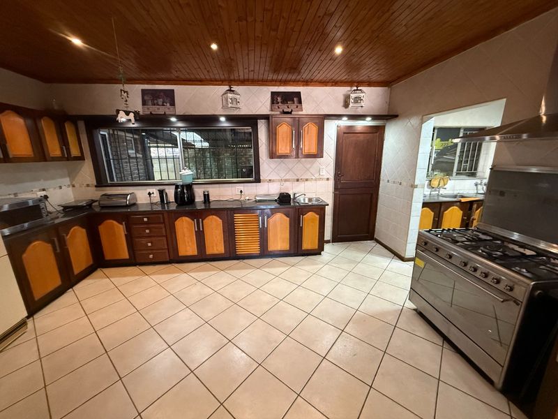 Spacious kitchen featuring timber ceilings, tiled flooring, built-in cabinetry, and a gas stove with extractor fan, with an adjacent scullery area.