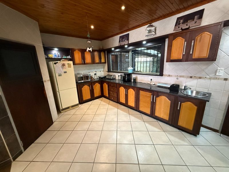 A functional kitchen featuring wooden ceiling panels, tiled flooring, granite countertops, and ample built-in cabinetry with a classic two-tone finish.